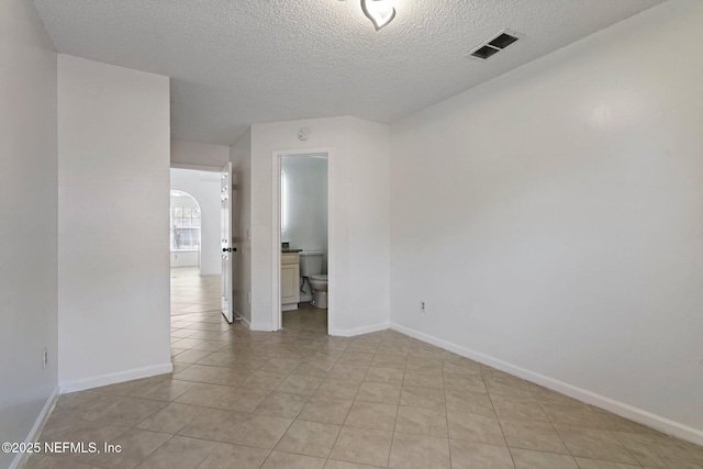 empty room with visible vents, a textured ceiling, arched walkways, light tile patterned floors, and baseboards