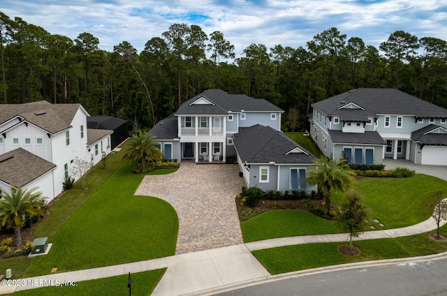 view of front of home featuring a front lawn, a balcony, a forest view, and driveway