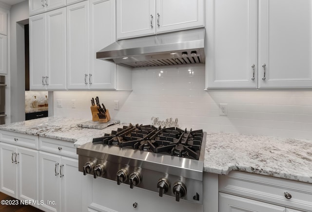 kitchen featuring decorative backsplash, stainless steel gas stovetop, light stone counters, and under cabinet range hood