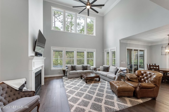 living area with ceiling fan with notable chandelier, crown molding, a fireplace, and wood-type flooring