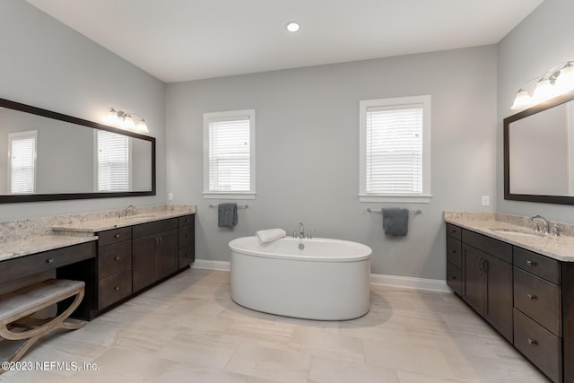 full bath featuring a sink, a freestanding tub, baseboards, and two vanities