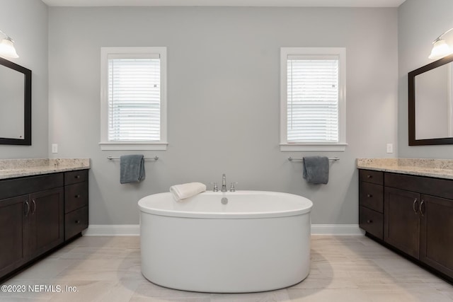 bathroom featuring a soaking tub, two vanities, a healthy amount of sunlight, and baseboards