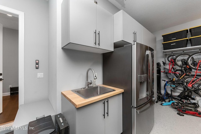 kitchen featuring white cabinets, butcher block countertops, stainless steel refrigerator with ice dispenser, and a sink