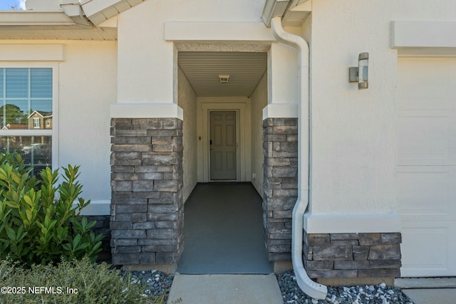 view of exterior entry with stucco siding, stone siding, and an attached garage