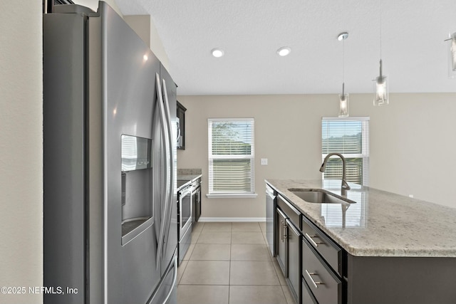 kitchen with light stone counters, light tile patterned floors, a center island with sink, a sink, and stainless steel appliances