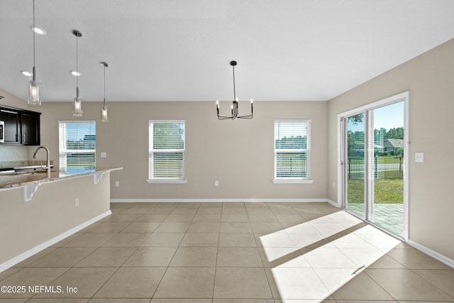 unfurnished dining area featuring a notable chandelier, light tile patterned floors, baseboards, and a sink