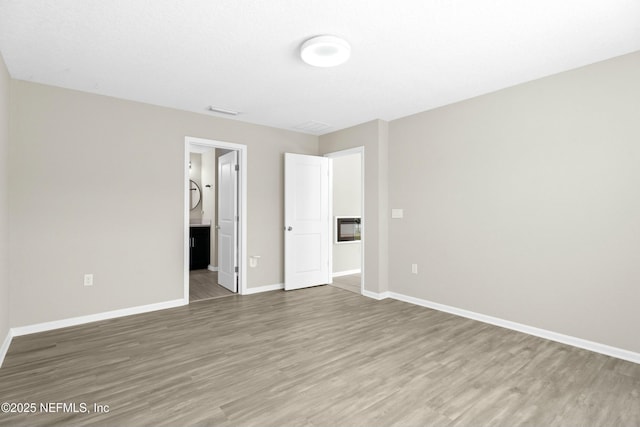 unfurnished bedroom with visible vents, connected bathroom, baseboards, and wood finished floors