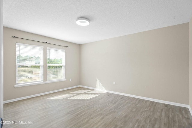 spare room with baseboards, a textured ceiling, and light wood-style flooring