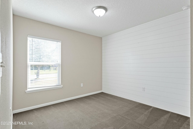 spare room featuring baseboards, dark colored carpet, and a textured ceiling