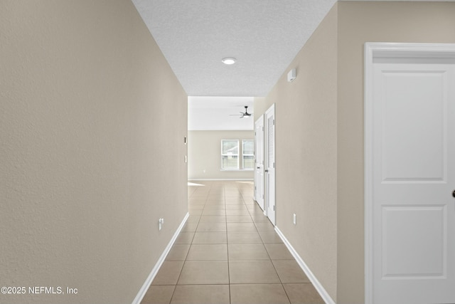 hallway featuring tile patterned floors, baseboards, and a textured ceiling