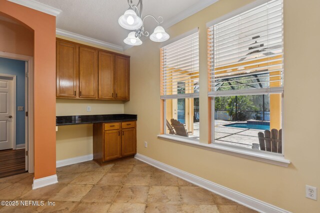 kitchen featuring ornamental molding, baseboards, brown cabinets, and built in study area