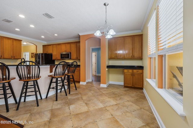 kitchen with stainless steel microwave, visible vents, a kitchen breakfast bar, freestanding refrigerator, and arched walkways