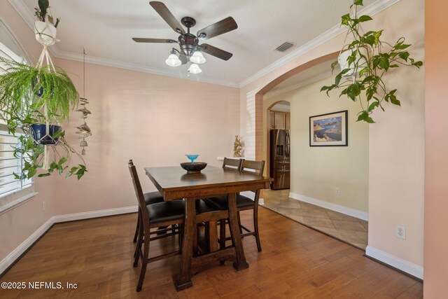 dining space with wood finished floors, arched walkways, and ornamental molding