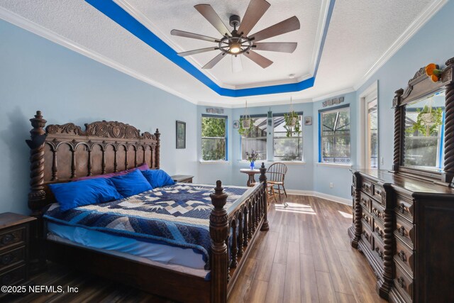 bedroom featuring a textured ceiling, crown molding, a tray ceiling, and wood finished floors