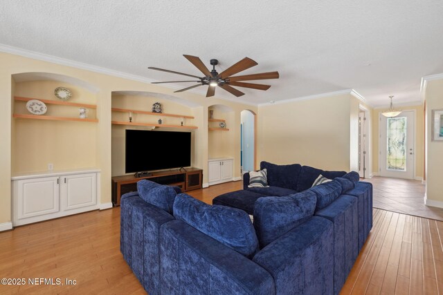 living area featuring light wood-type flooring, built in features, a textured ceiling, arched walkways, and crown molding