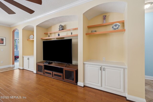 living room with built in features, light wood finished floors, ceiling fan, a textured ceiling, and crown molding