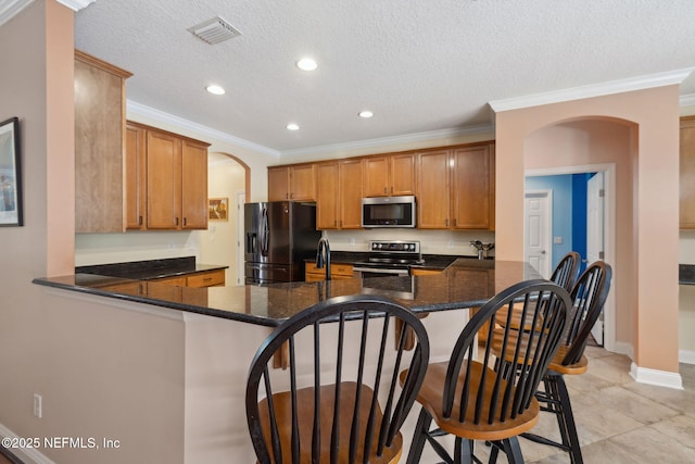 kitchen featuring visible vents, brown cabinetry, a peninsula, arched walkways, and stainless steel appliances