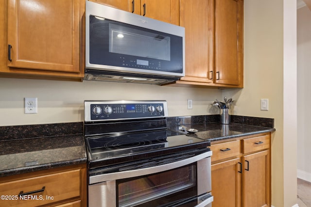 kitchen featuring stainless steel appliances, baseboards, brown cabinetry, and dark stone counters