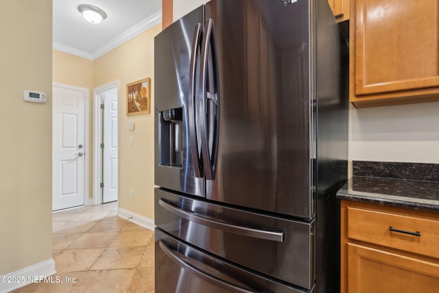 kitchen featuring dark stone countertops, baseboards, brown cabinets, crown molding, and stainless steel fridge