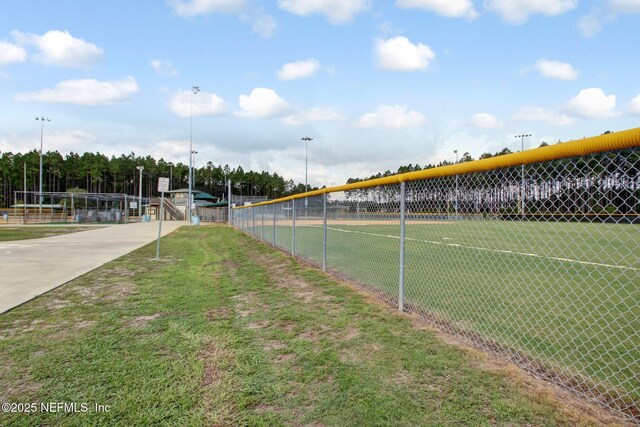 view of tennis court with a lawn and fence