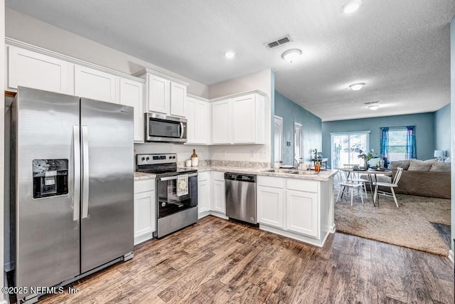 kitchen featuring visible vents, open floor plan, stainless steel appliances, white cabinetry, and a sink