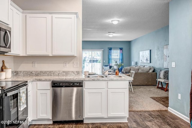 kitchen with a sink, open floor plan, appliances with stainless steel finishes, white cabinets, and light countertops