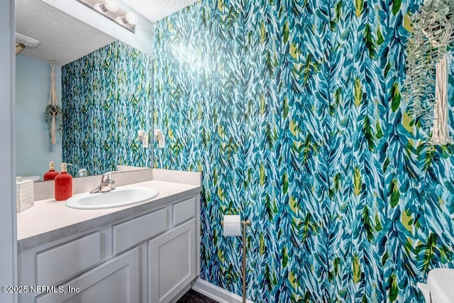 bathroom featuring vanity, wallpapered walls, and a textured ceiling