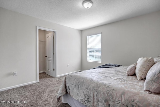 bedroom with a walk in closet, baseboards, a textured ceiling, and carpet flooring