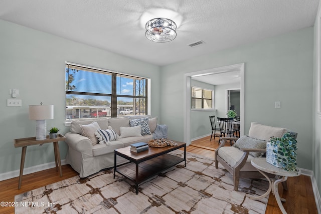 living area featuring visible vents, baseboards, a textured ceiling, and light wood-style flooring