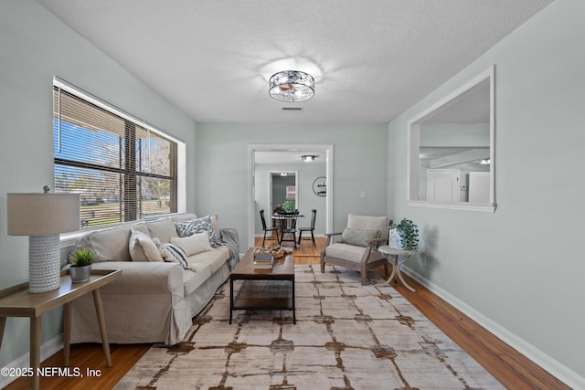 living room with visible vents, a textured ceiling, baseboards, and wood finished floors