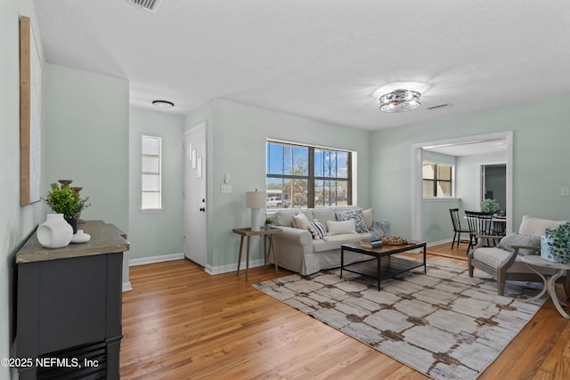 living area featuring baseboards, visible vents, light wood finished floors, and a textured ceiling