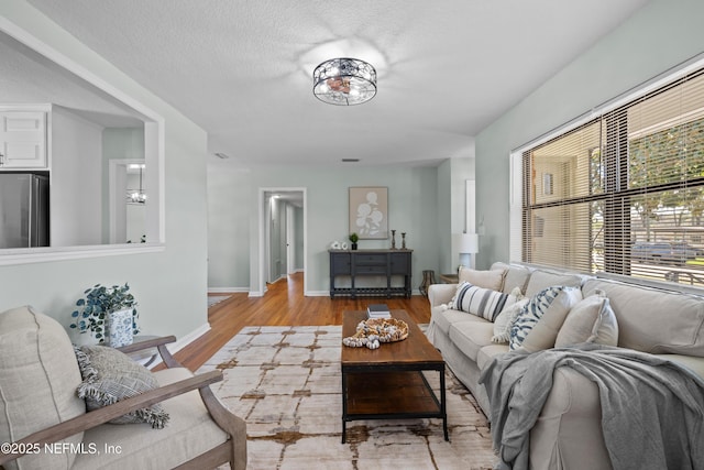 living area featuring baseboards, a textured ceiling, and light wood finished floors