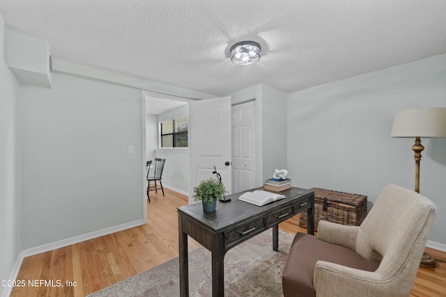 home office with a textured ceiling, light wood-type flooring, and baseboards