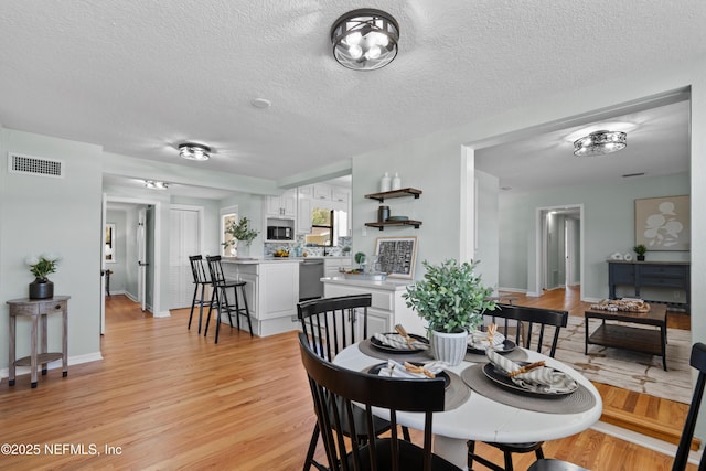 dining space with visible vents, light wood-style flooring, a textured ceiling, and baseboards