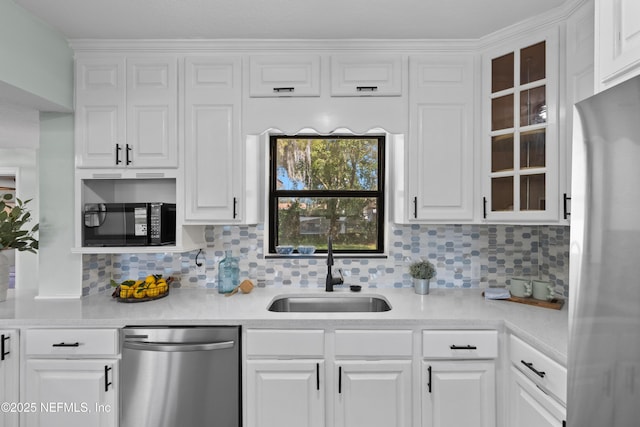 kitchen with a sink, appliances with stainless steel finishes, white cabinets, light countertops, and glass insert cabinets