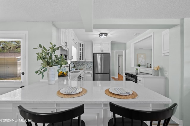 kitchen featuring a sink, stainless steel fridge, a peninsula, glass insert cabinets, and range