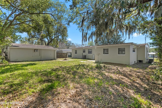 back of property with central air condition unit, a lawn, and fence