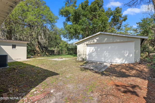 view of yard featuring central air condition unit, a detached garage, and an outdoor structure