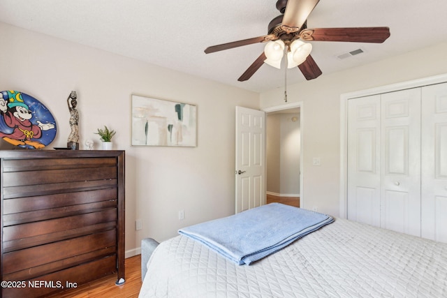 bedroom featuring a ceiling fan, wood finished floors, visible vents, baseboards, and a closet