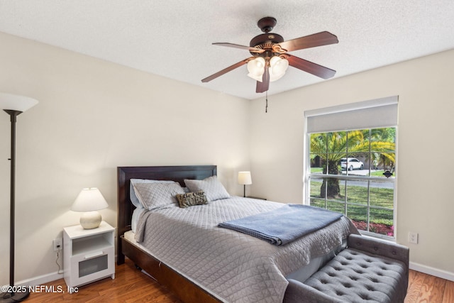 bedroom featuring a ceiling fan, wood finished floors, baseboards, and a textured ceiling