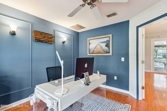 office featuring visible vents, a textured ceiling, wood finished floors, and a ceiling fan