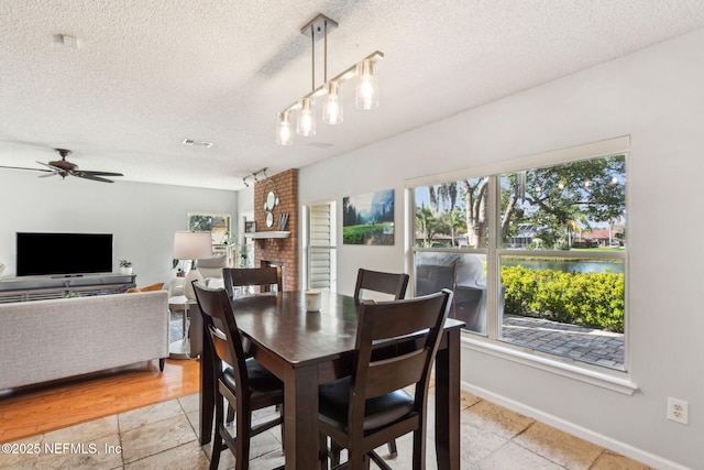 dining room featuring visible vents, baseboards, ceiling fan, a water view, and a textured ceiling