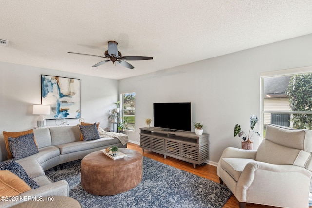 living area with visible vents, a ceiling fan, a textured ceiling, wood finished floors, and baseboards