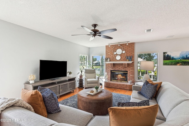 living area with visible vents, ceiling fan, a fireplace, wood finished floors, and a textured ceiling