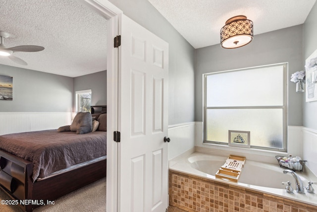 full bathroom featuring a wainscoted wall, a textured ceiling, and ceiling fan