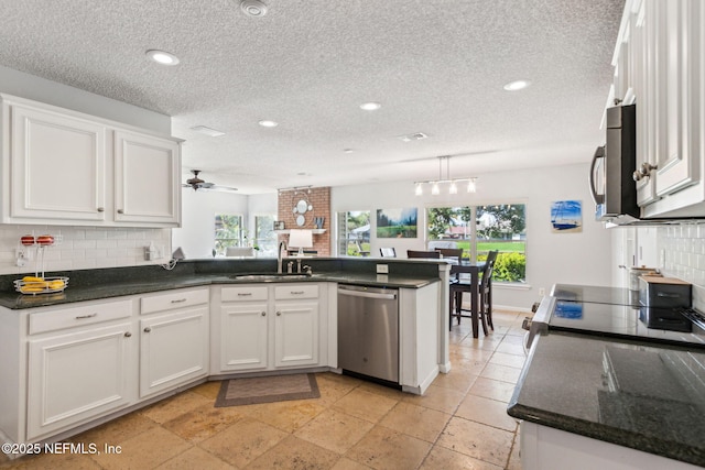 kitchen featuring backsplash, appliances with stainless steel finishes, a peninsula, white cabinets, and a sink