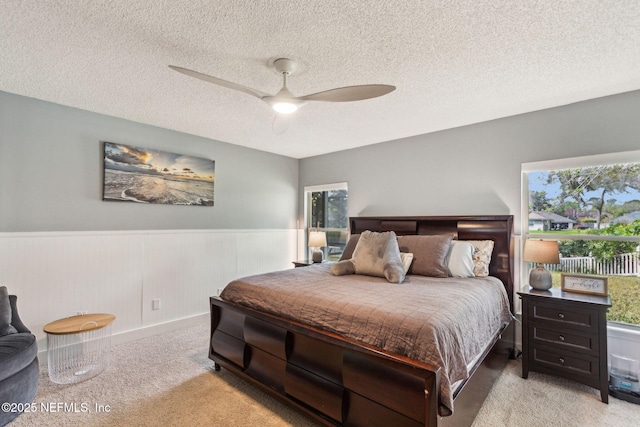 bedroom with light carpet, a wainscoted wall, a textured ceiling, and a ceiling fan