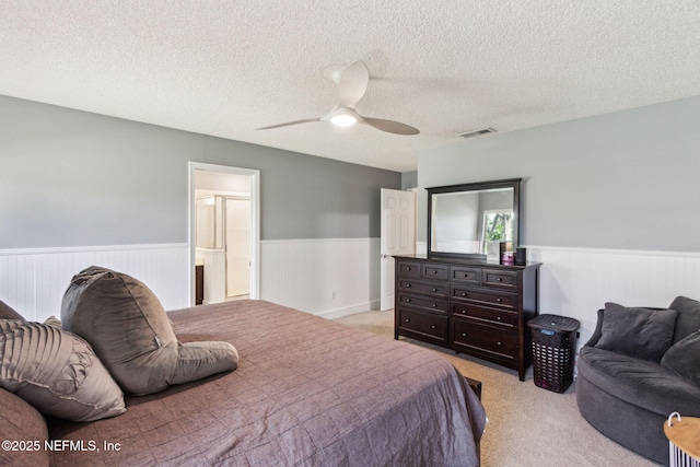 bedroom with visible vents, wainscoting, a textured ceiling, and light colored carpet