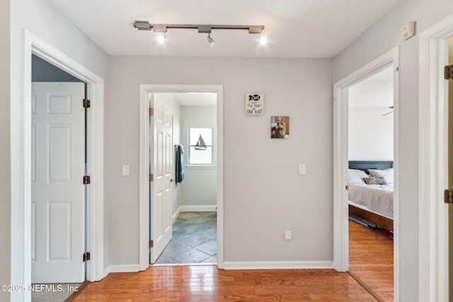 hall with baseboards, a textured ceiling, and light wood finished floors