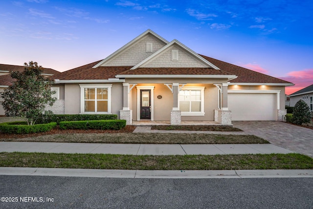 craftsman-style home featuring stucco siding, a shingled roof, decorative driveway, and a garage